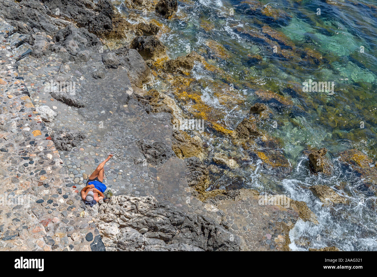 Single man sunbathing alone on a rocky beach, on the historic Peloponnese, island of Momenvasia in Greece. Stock Photo