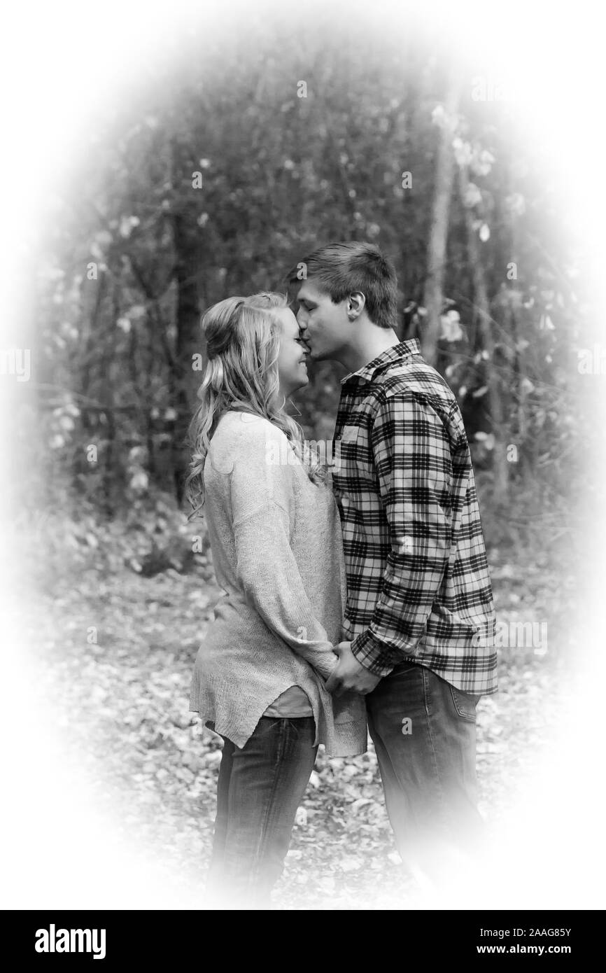 Man kissing his girlfriend on top of the head in a park in B&W Stock Photo