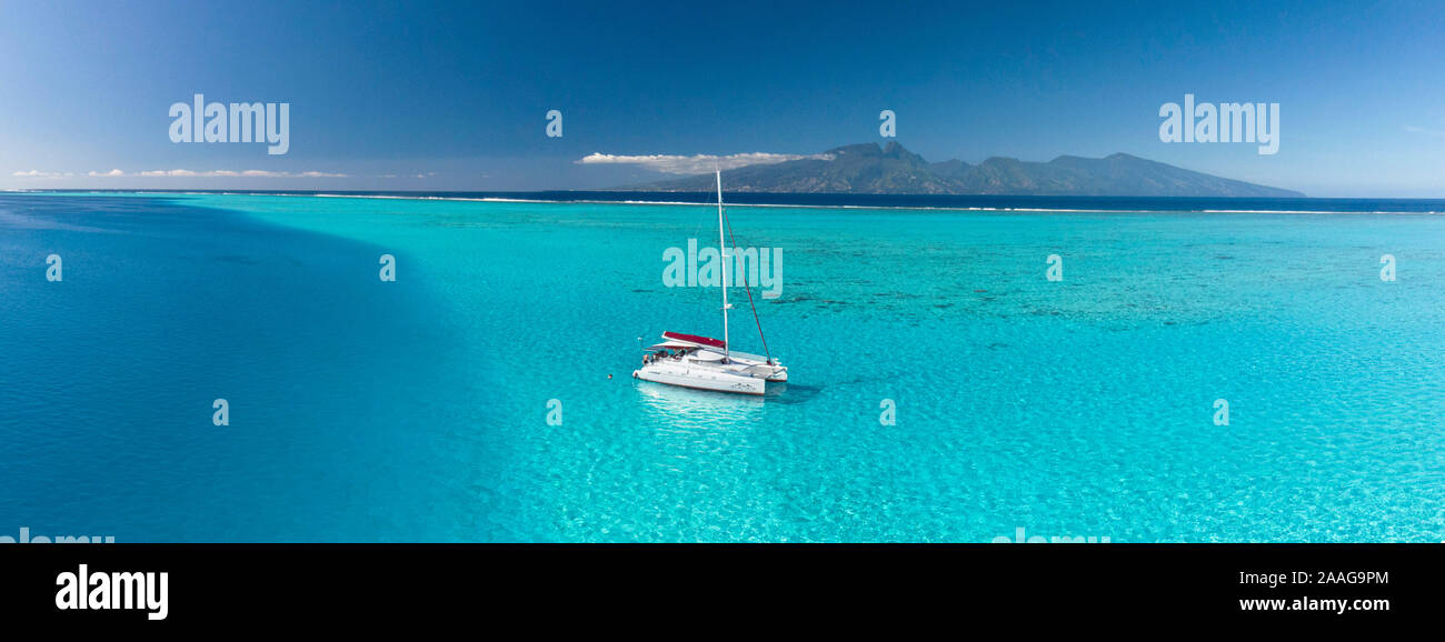 Sailing catamaran anchored in the lagoon of Moorea, with Tahiti Island in the background. Picture taken by drone. Stock Photo