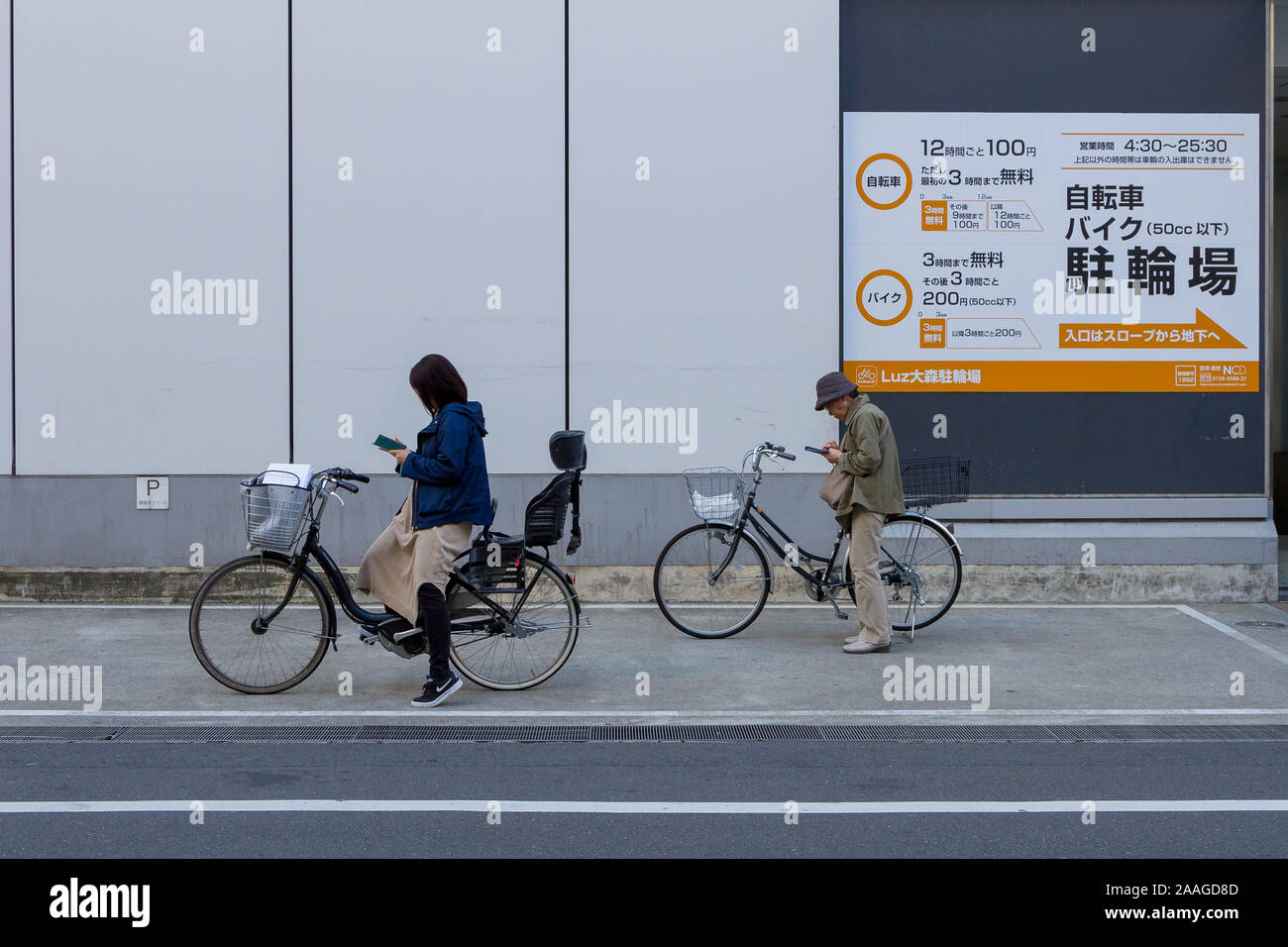 Women stands by thier bicycles to use smartphones in a street Omori, Tokyo, Japan Stock Photo
