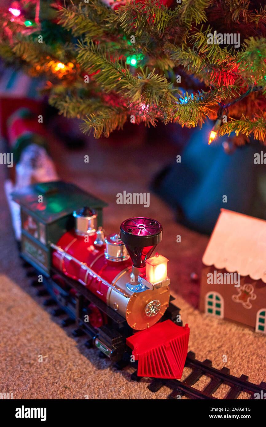 A toy model train on tracks and a gingerbread house under a Christmas tree with lights and decorations for the holiday season. Stock Photo