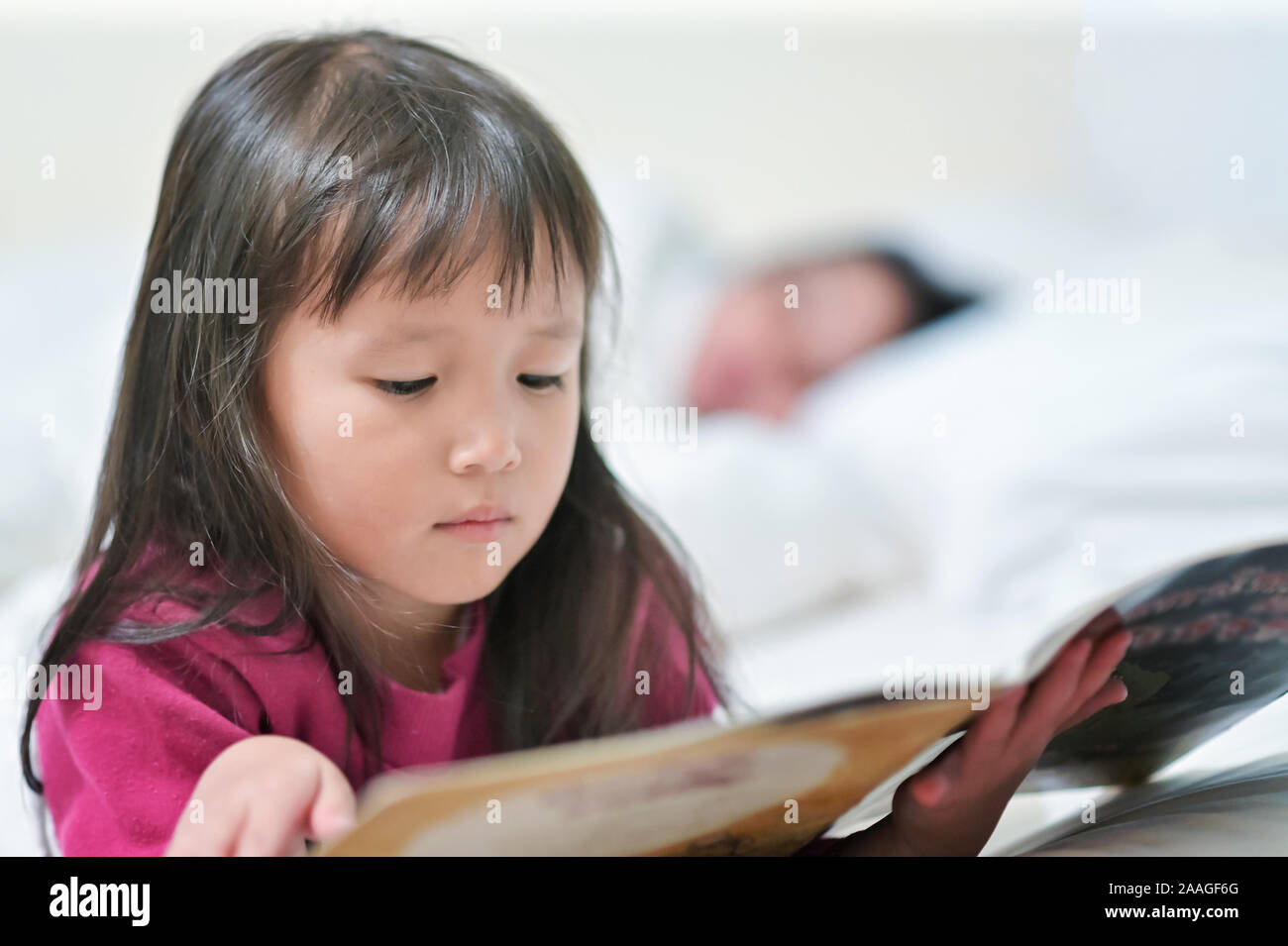 Asian little girl reading a tale book on bed before sleep in the bedroom Stock Photo