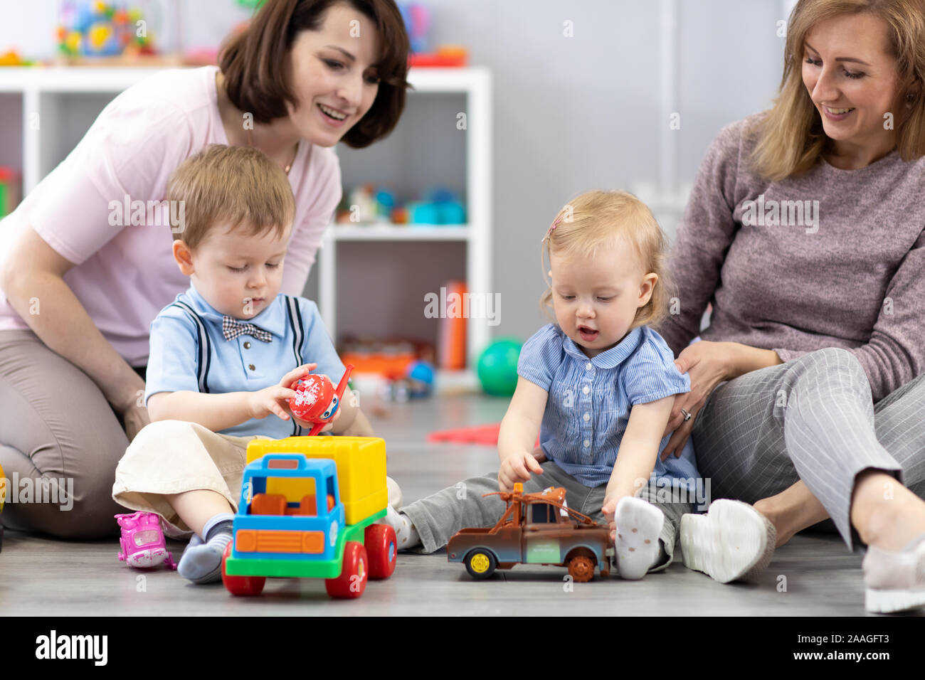 Happy two mothers with their children play at home or daycare interior Stock Photo