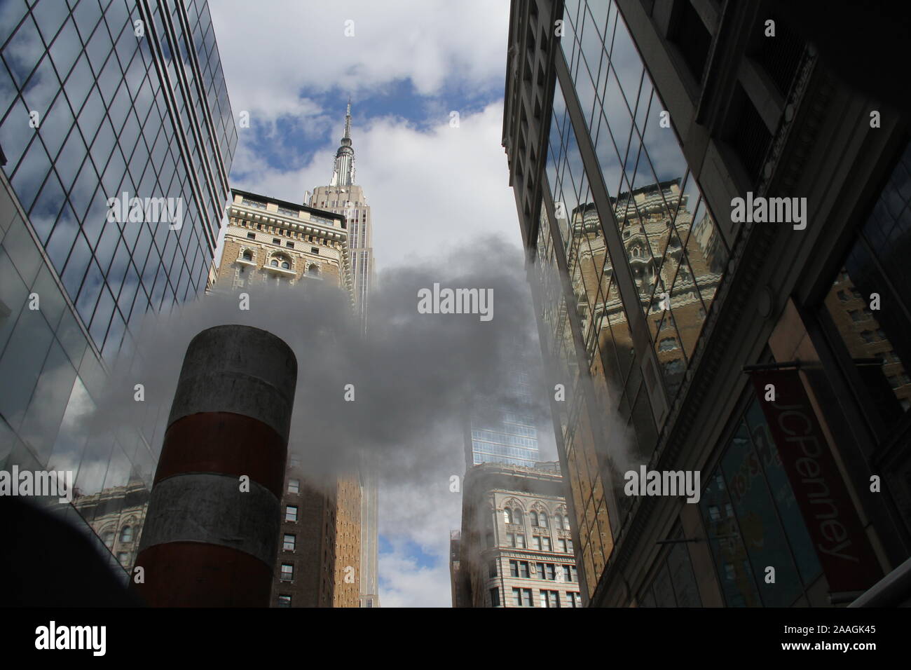 Subway steam clouds rising between Manhattan skyscrapers, towards the Empire State Building against blue sky with white clouds Stock Photo