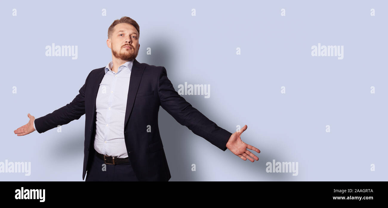 Handsome bearded man with open arms in a suit without a tie. Studio portrait over gray blue background. Stock Photo