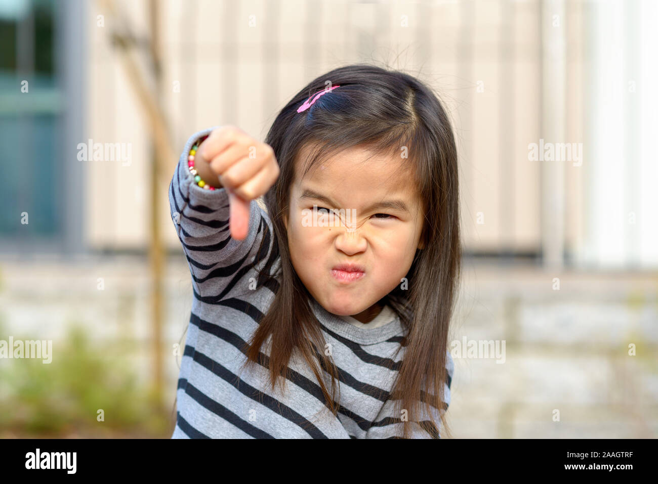 Angry little Asian girl punching her fist at the camera while pulling a fierce face in a show of childish aggression Stock Photo