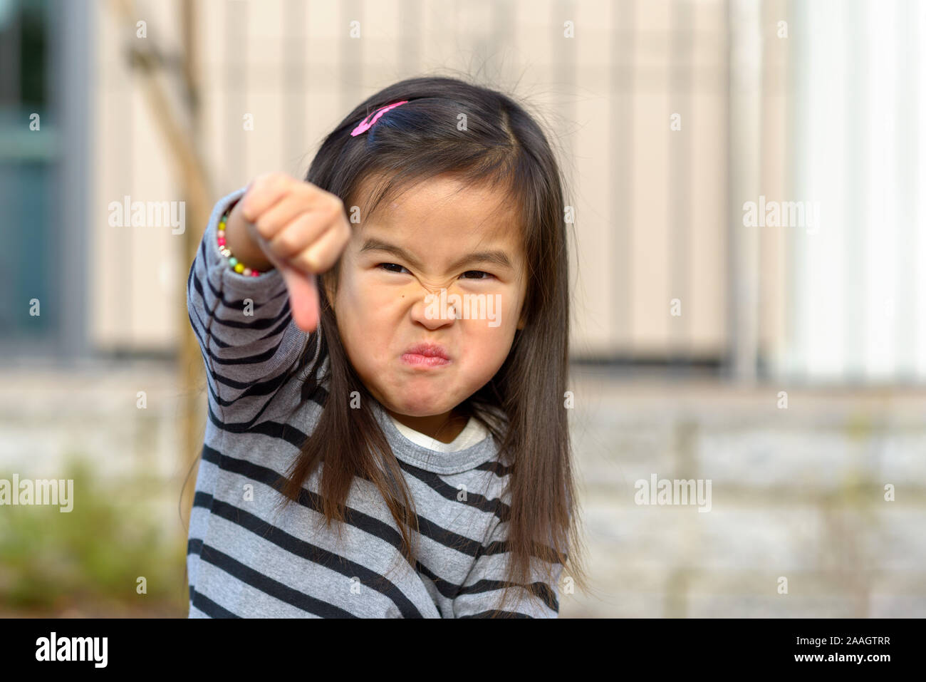 Angry frustrated little girl throwing a temper tantrum punching her fist at the camera with a furious vengeful expression outdoors Stock Photo