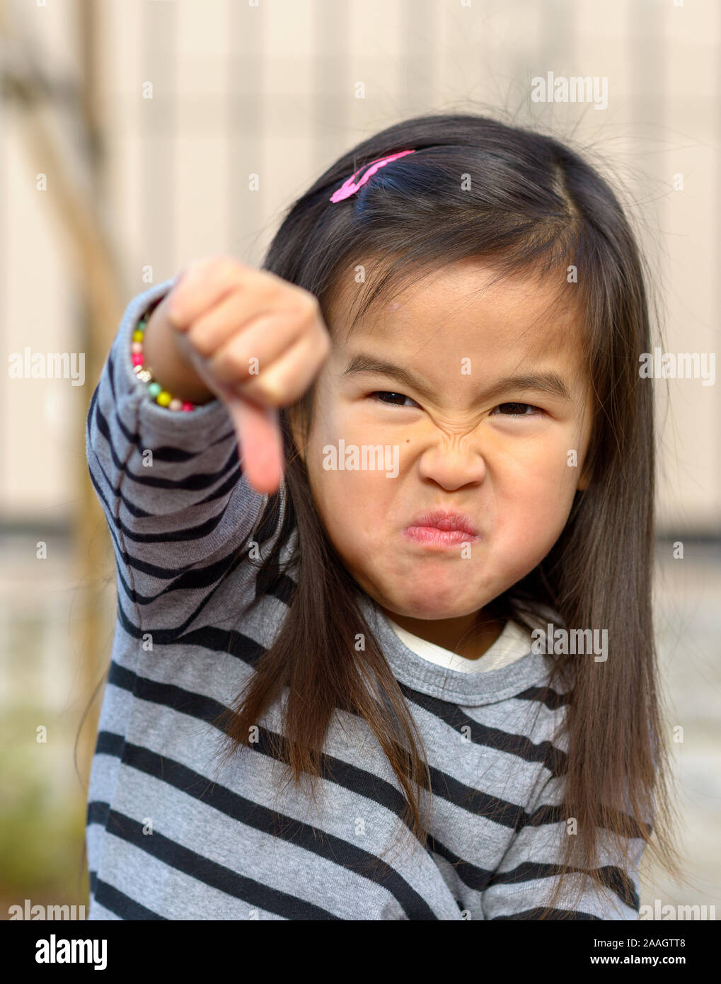 Portrait of angry frustrated little girl throwing a thumb down gesture at the camera with a furious vengeful expression outdoors Stock Photo