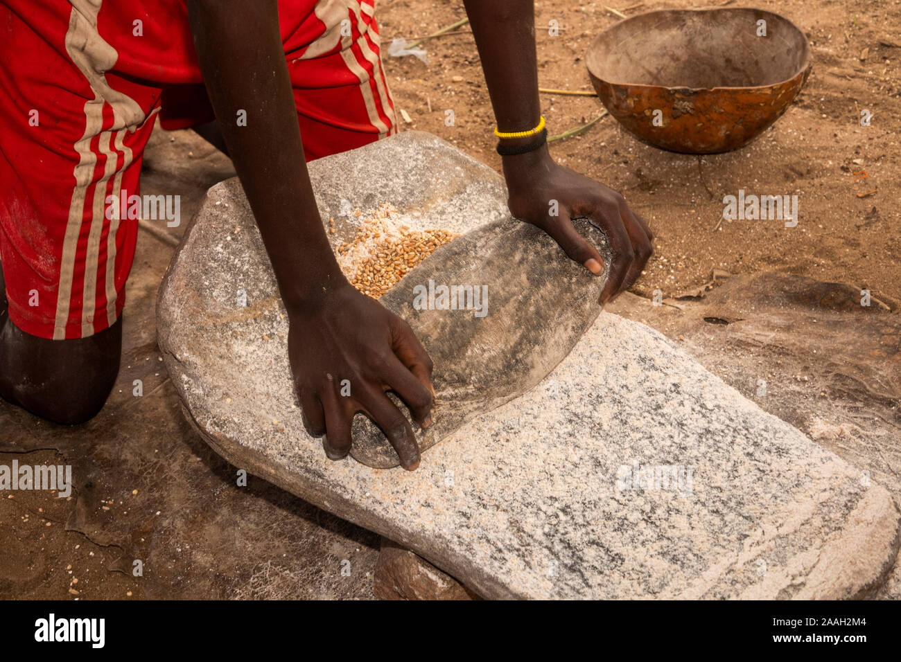 Ethiopia, South Omo, Kolcho village, hands of young girl grinding grain on stone to make flour Stock Photo