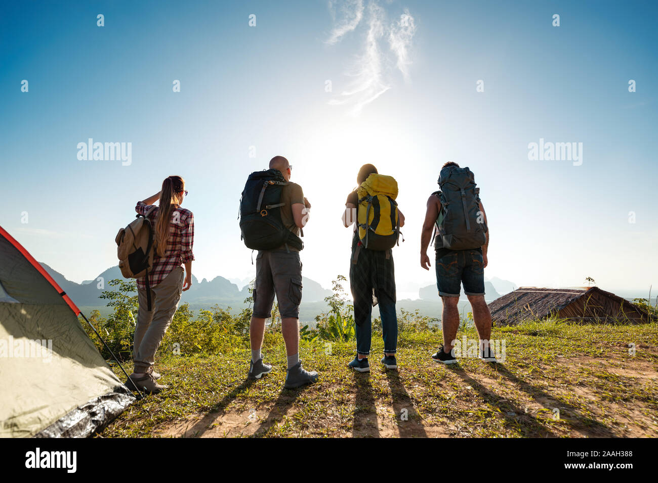 Group of four young hikers stands near tent and looks at sunrise and islands Stock Photo
