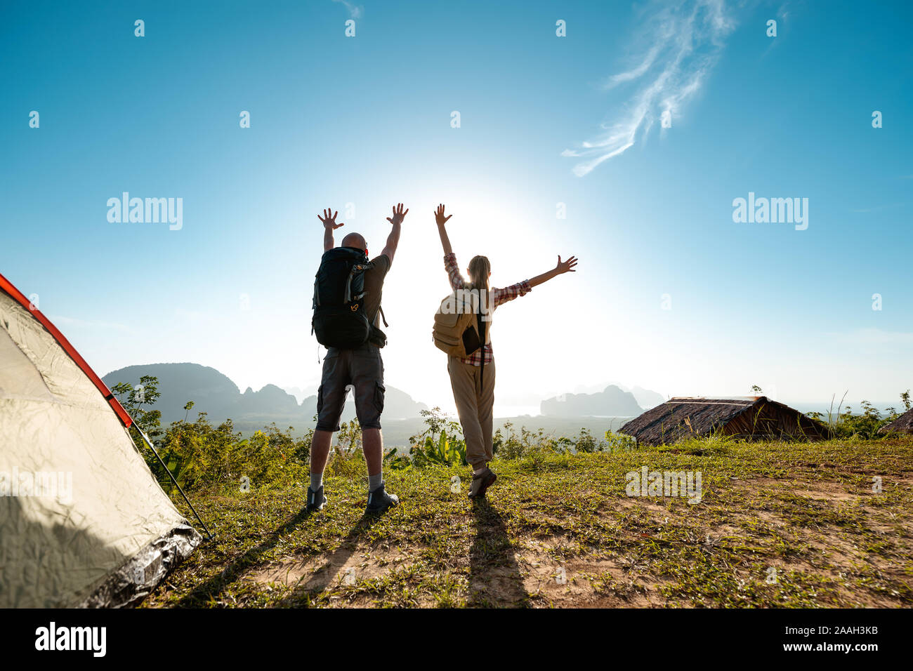 Two happy hikers male and female stands with raised arms at sunrise near tent Stock Photo
