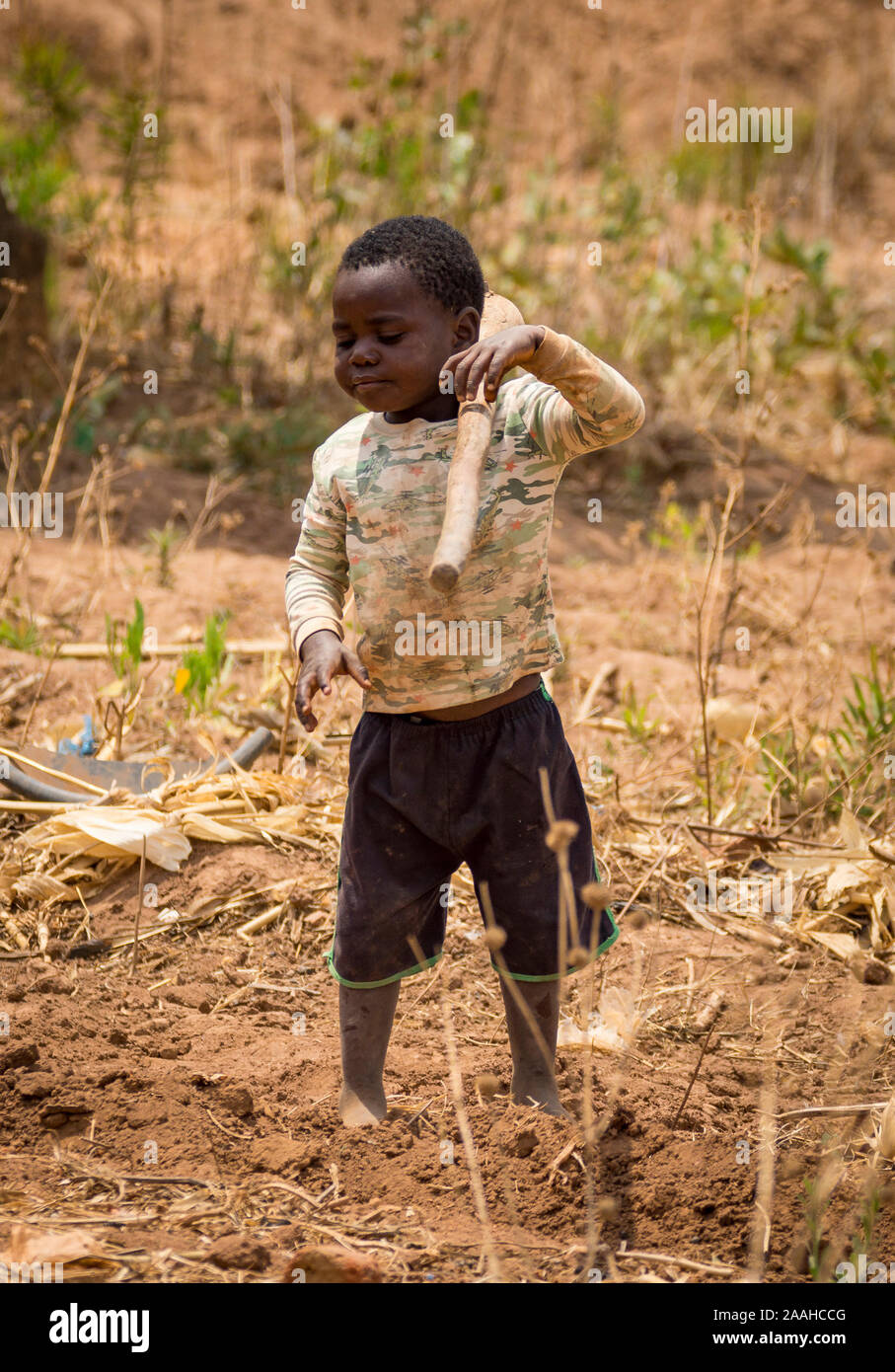 A young child in a rural village in Malawi picks up a hoe Stock Photo