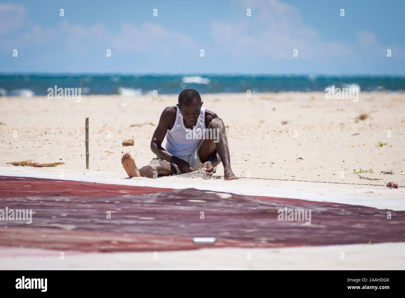 A lone man on the shore of Lake Malawi mends his fishing net Stock Photo