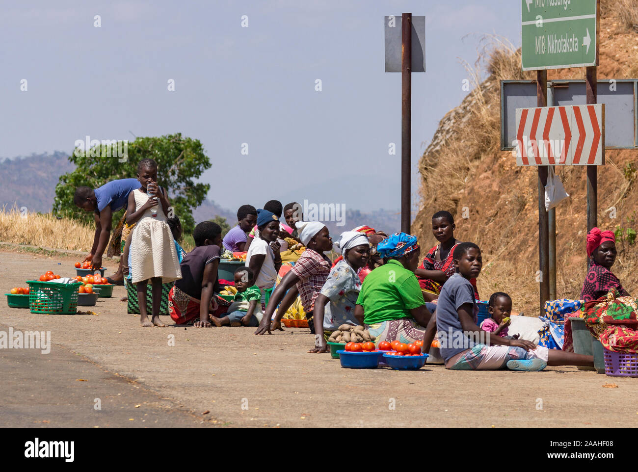 A group of women street vendors wait by the roadside for trade from passing vehicles in Malawi Stock Photo