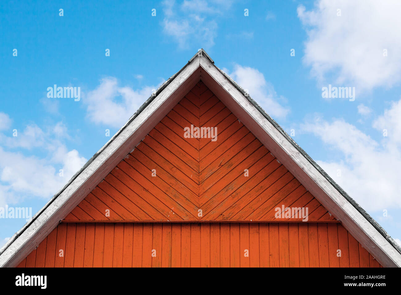 Red wooden gable under blue cloudy sky, rural Scandinavian architecture background Stock Photo