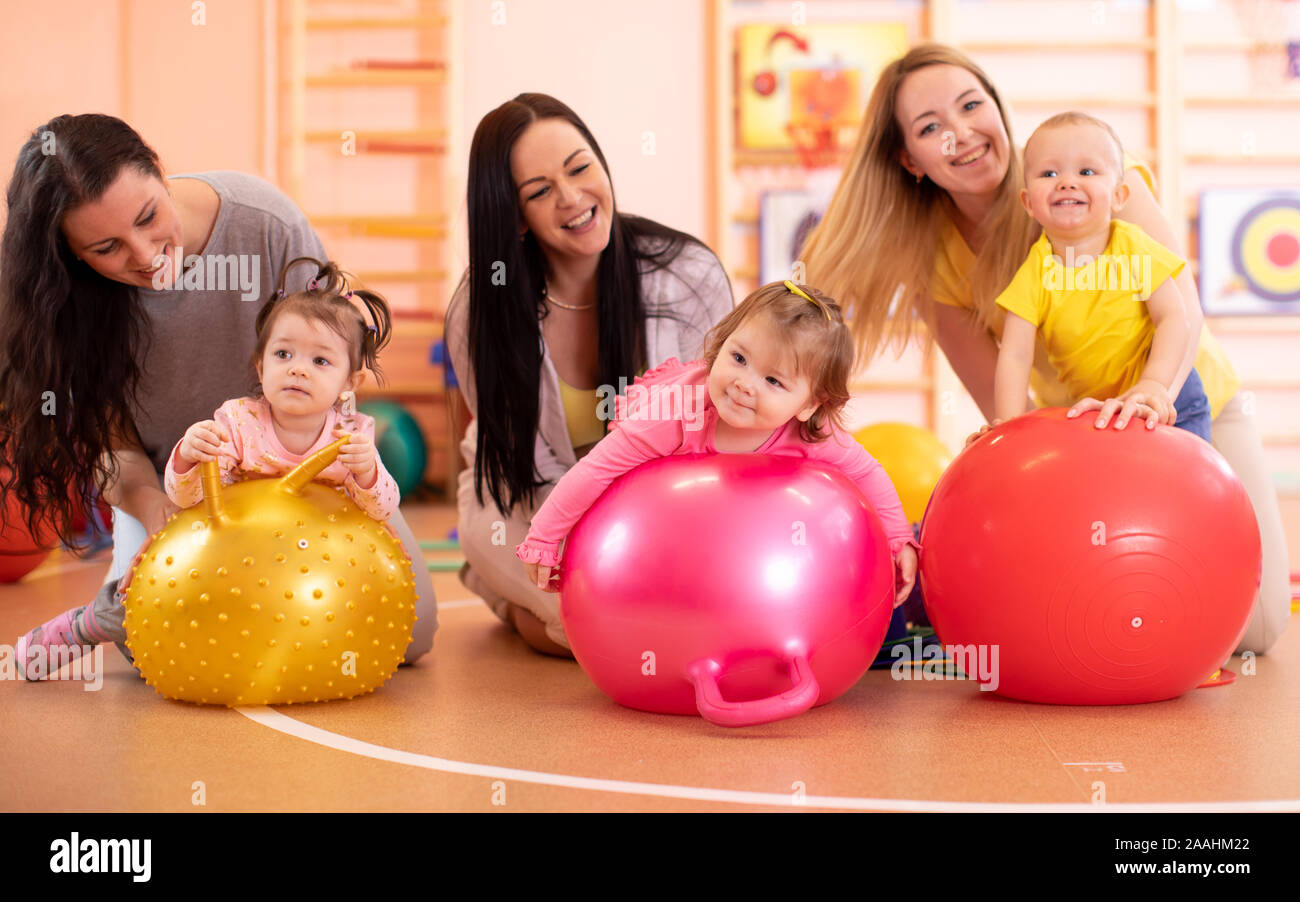 Group of mothers and their kids doing yoga exercises on gymnastic balls at fitness gym Stock Photo