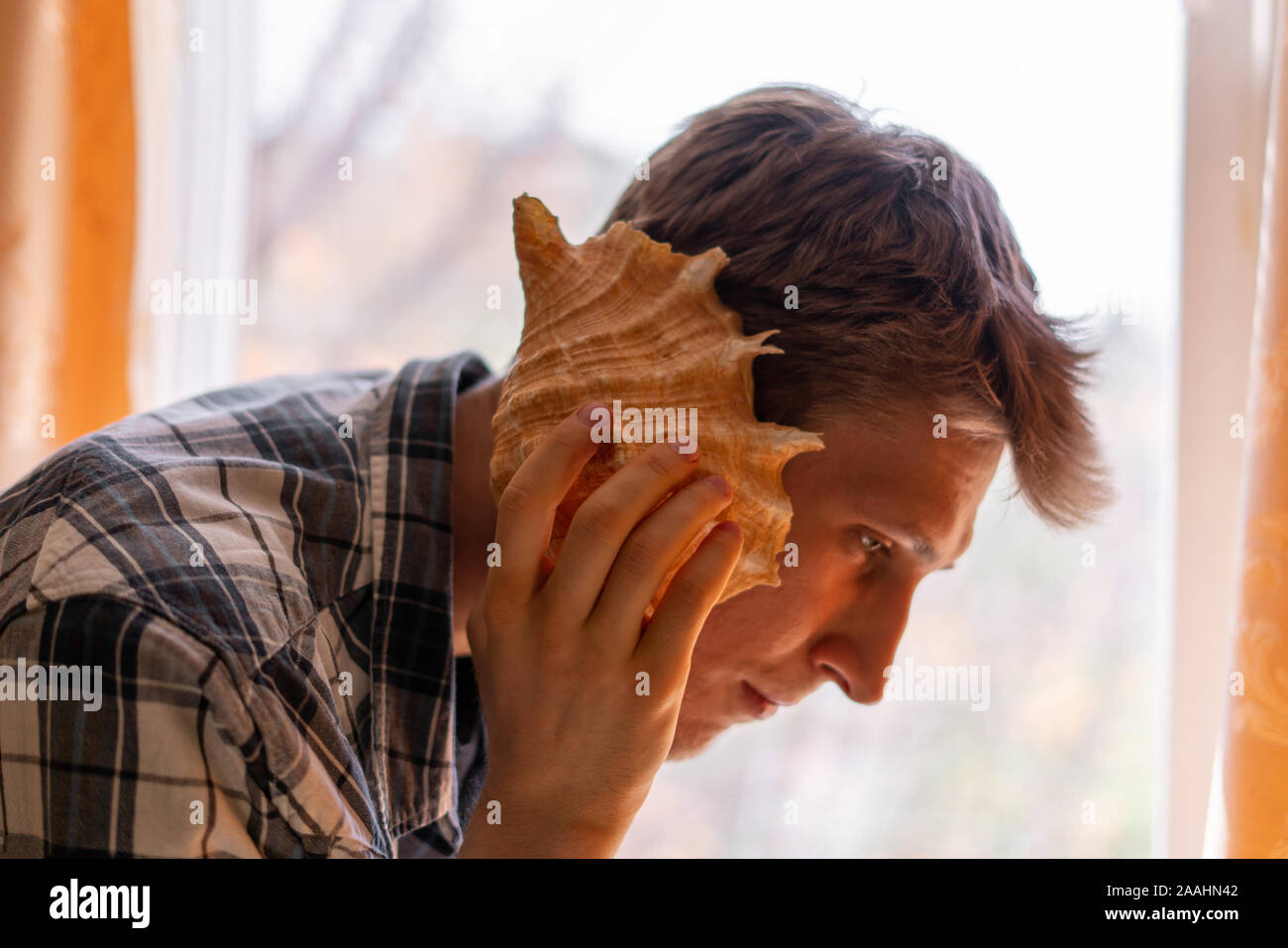 male person holding a sea shell to the hear, dreaming and hearing