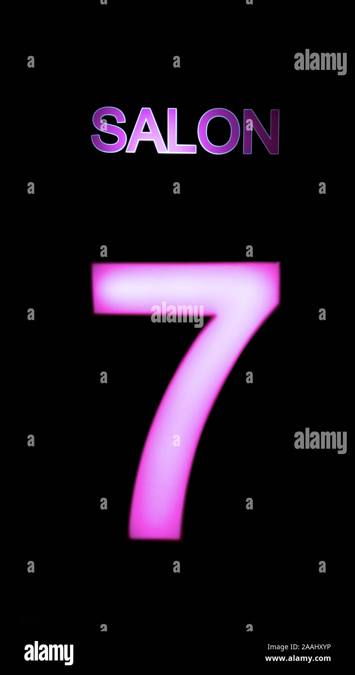 Front view of pink illuminated number 7 symbol and salon marquee signs on black background. Stock Photo
