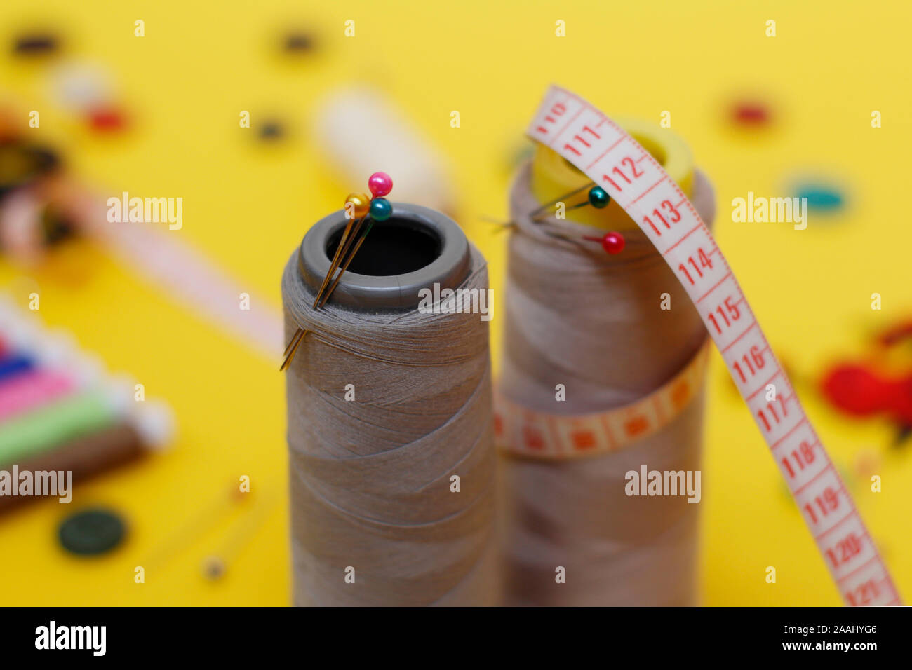 Sewing buttons and threads on a yellow background. Needlework concept. A lot of multi-colored little bobbins of sewing thread on a yellow background. Stock Photo