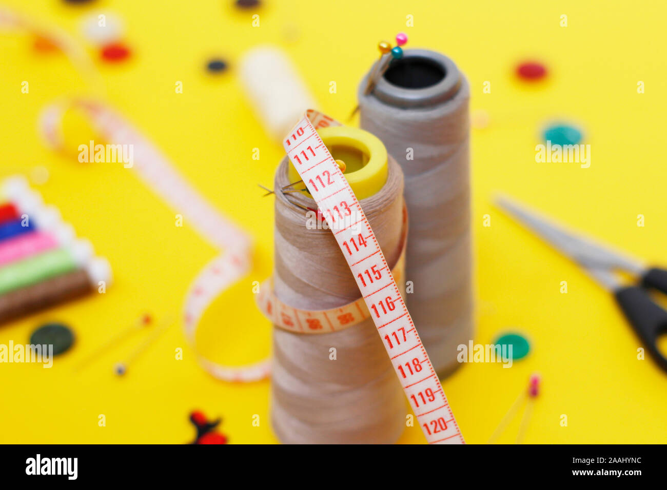 Sewing buttons and threads on a yellow background. Needlework concept. A lot of multi-colored little bobbins of sewing thread on a yellow background. Stock Photo