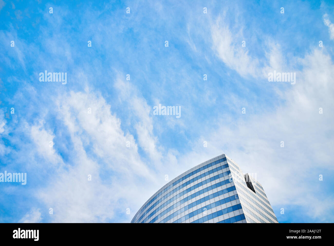 The top of a modern skyscraper or commercial building with glass windows and blue sky with clouds in the background Stock Photo