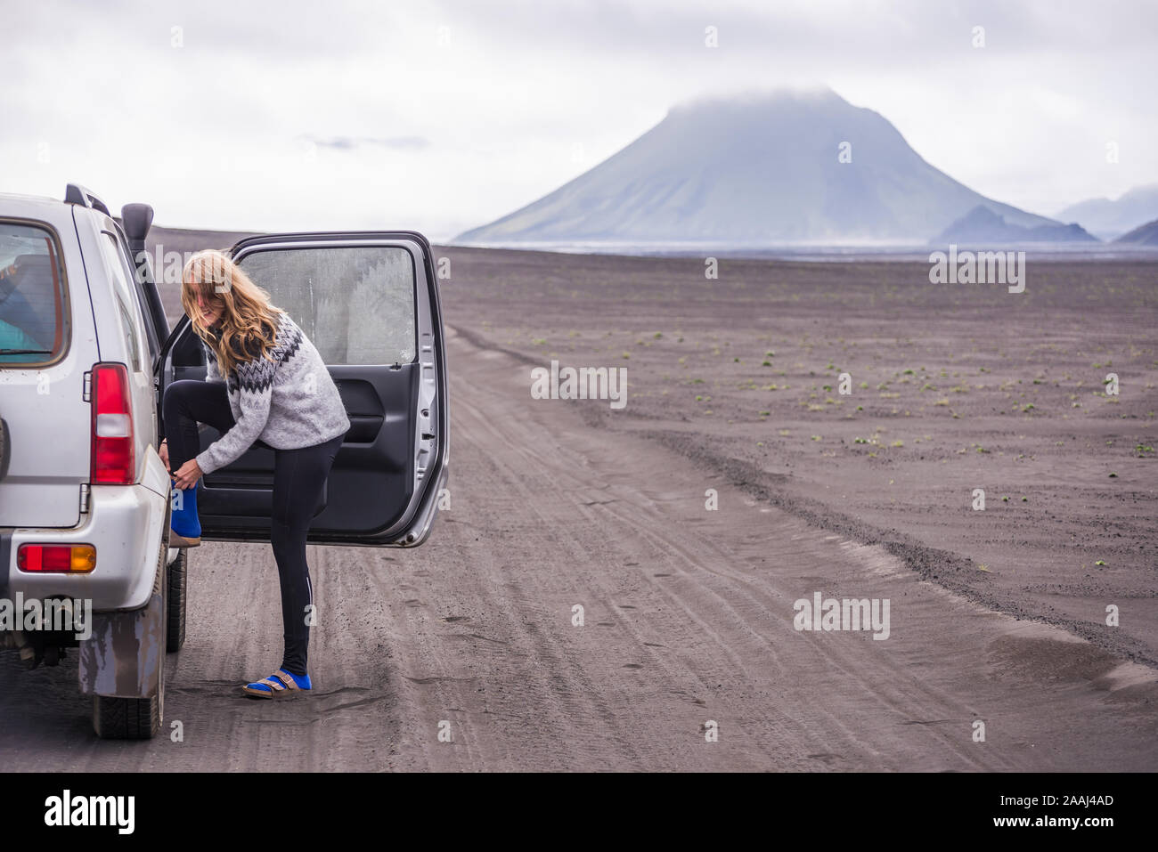 Woman changing shoes by vehicle door on dirt track, Landmannalaugar, Iceland Stock Photo