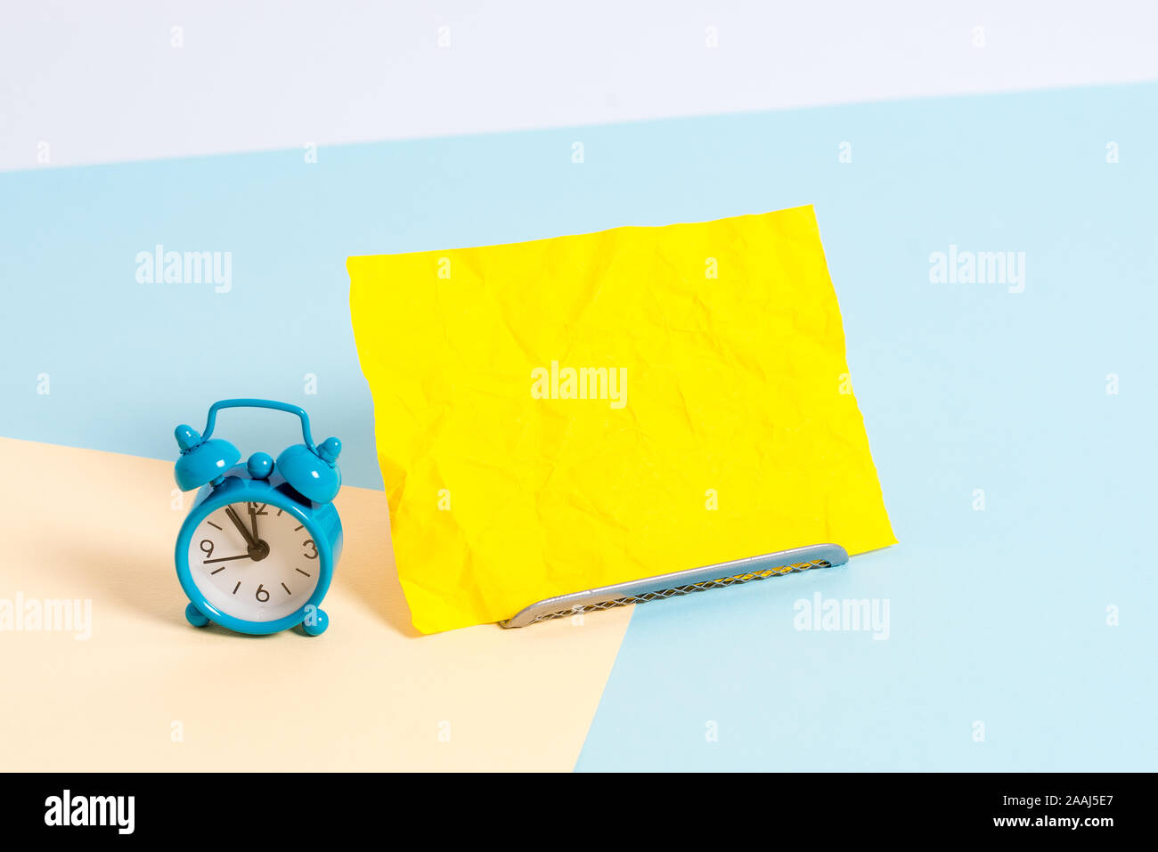 Mini size alarm clock beside a Paper sheet placed tilted on pastel