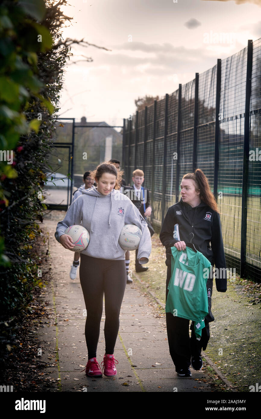 A netball player and her games teacher return from the court at a secondary school in the late afternoon light, UK Stock Photo