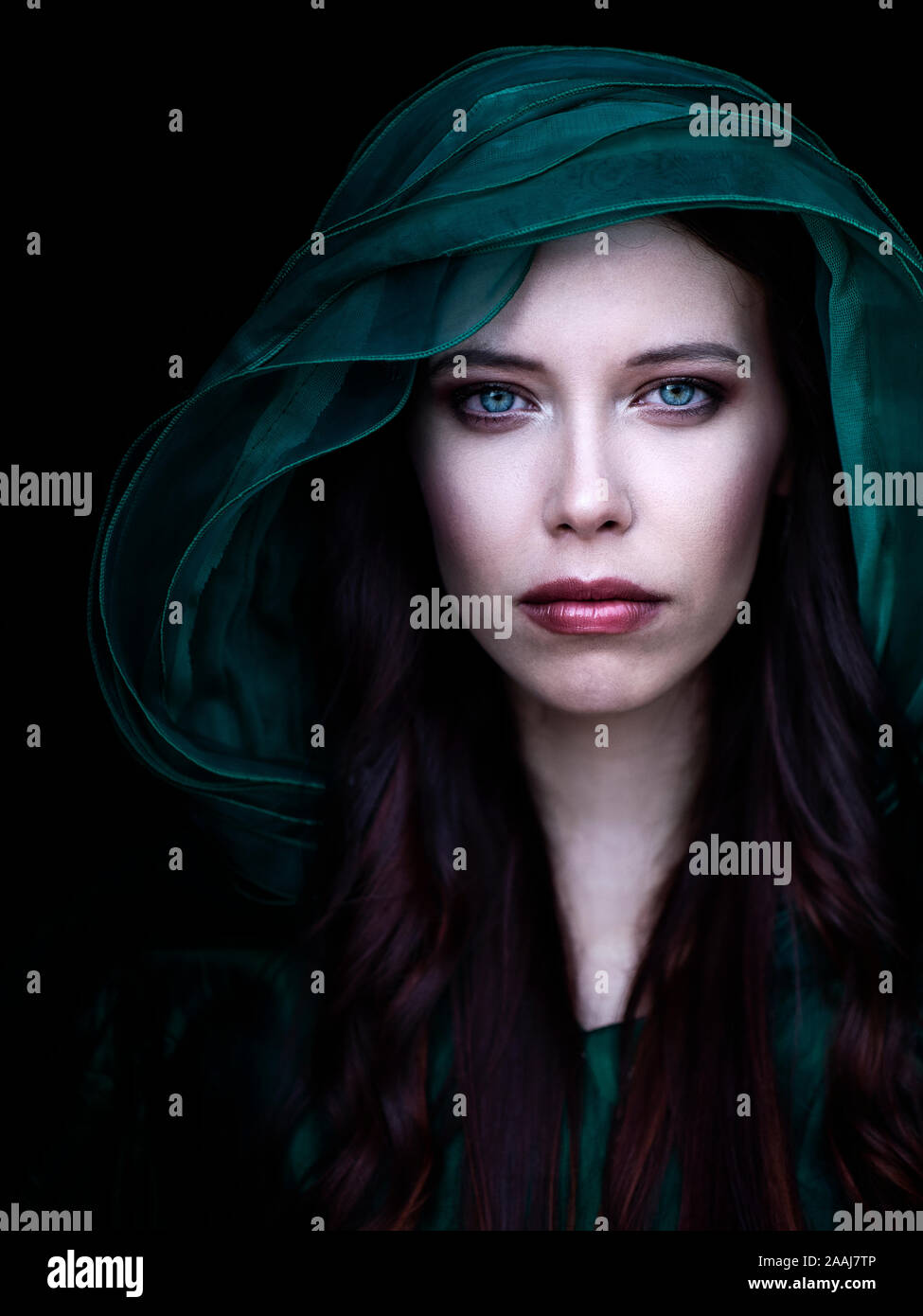 Stunningly beautiful young woman with blue eyes and long red hair looking at camera, wearing red hood Stock Photo