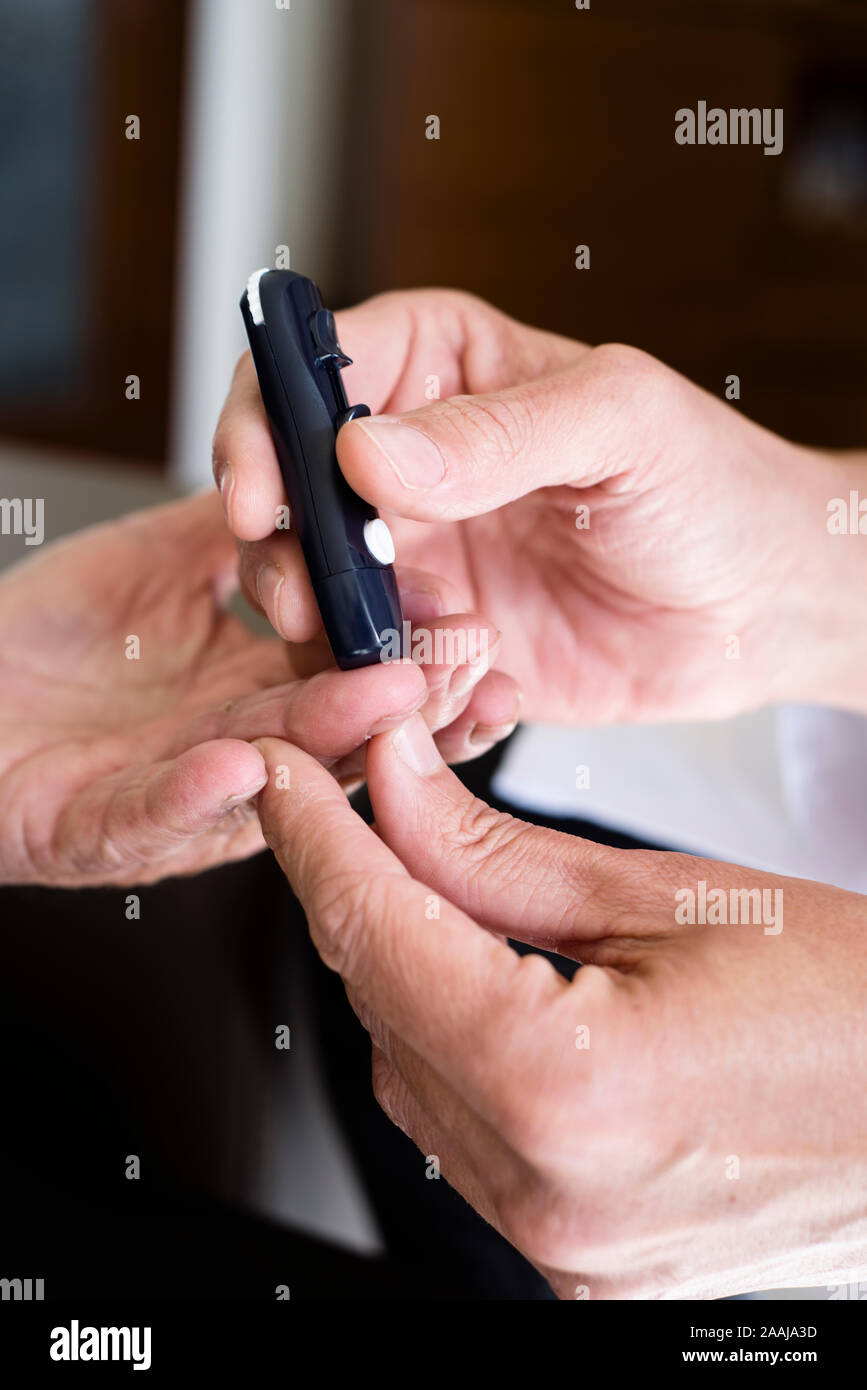 closeup of a young caucasian medic man wearing a white coat about to measure the blood glucose level of an old caucasian man, in a glucose meter, by p Stock Photo