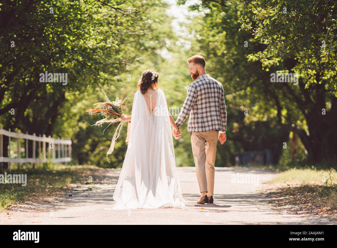 Happy bride and groom holding hands and walking in garden wedding day ...