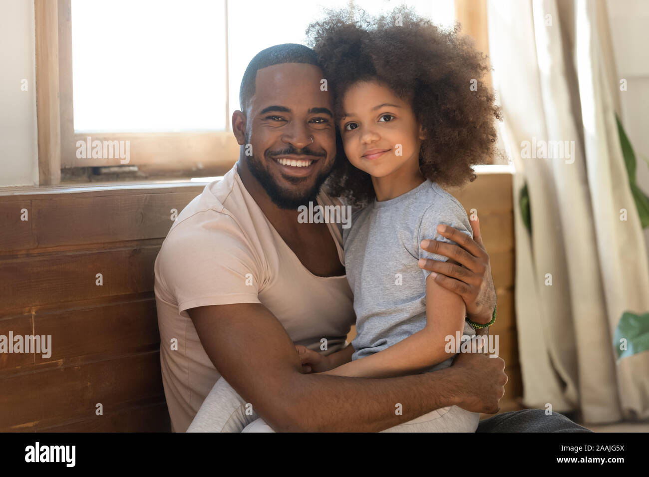Smiling biracial dad and preschooler daughter hug looking at camera Stock Photo