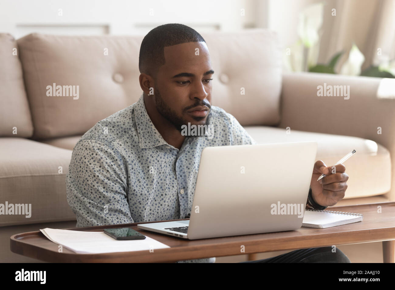 Focused biracial man studying at laptop making notes Stock Photo