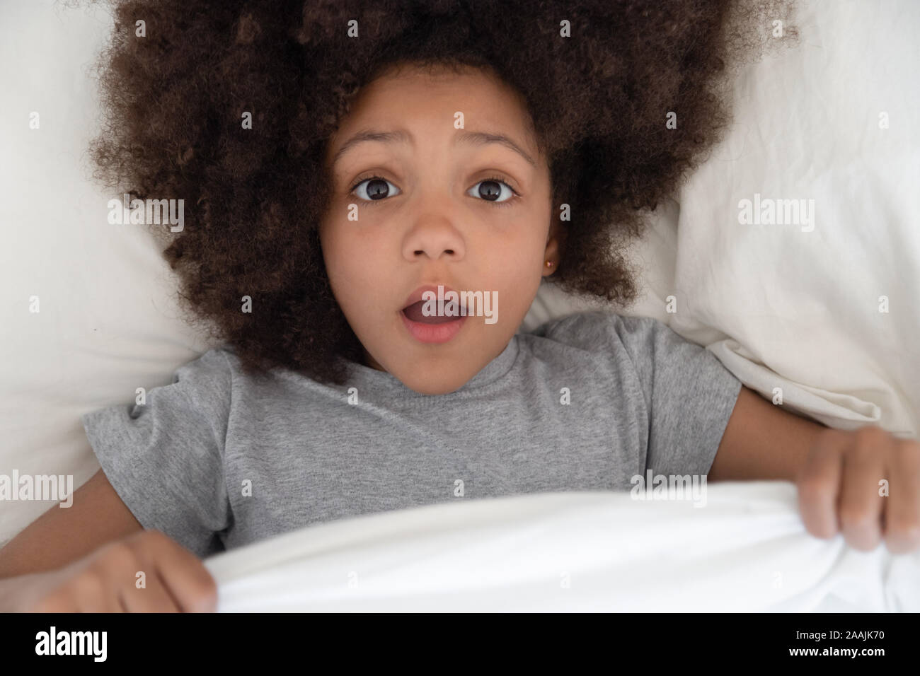Scared biracial small girl peek from duvet having bad dream Stock Photo