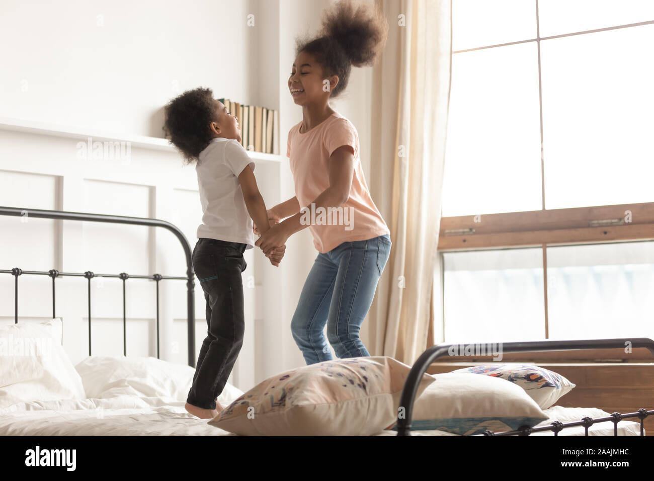 Mixed-race brother and sister holding hands jumping on bed Stock Photo