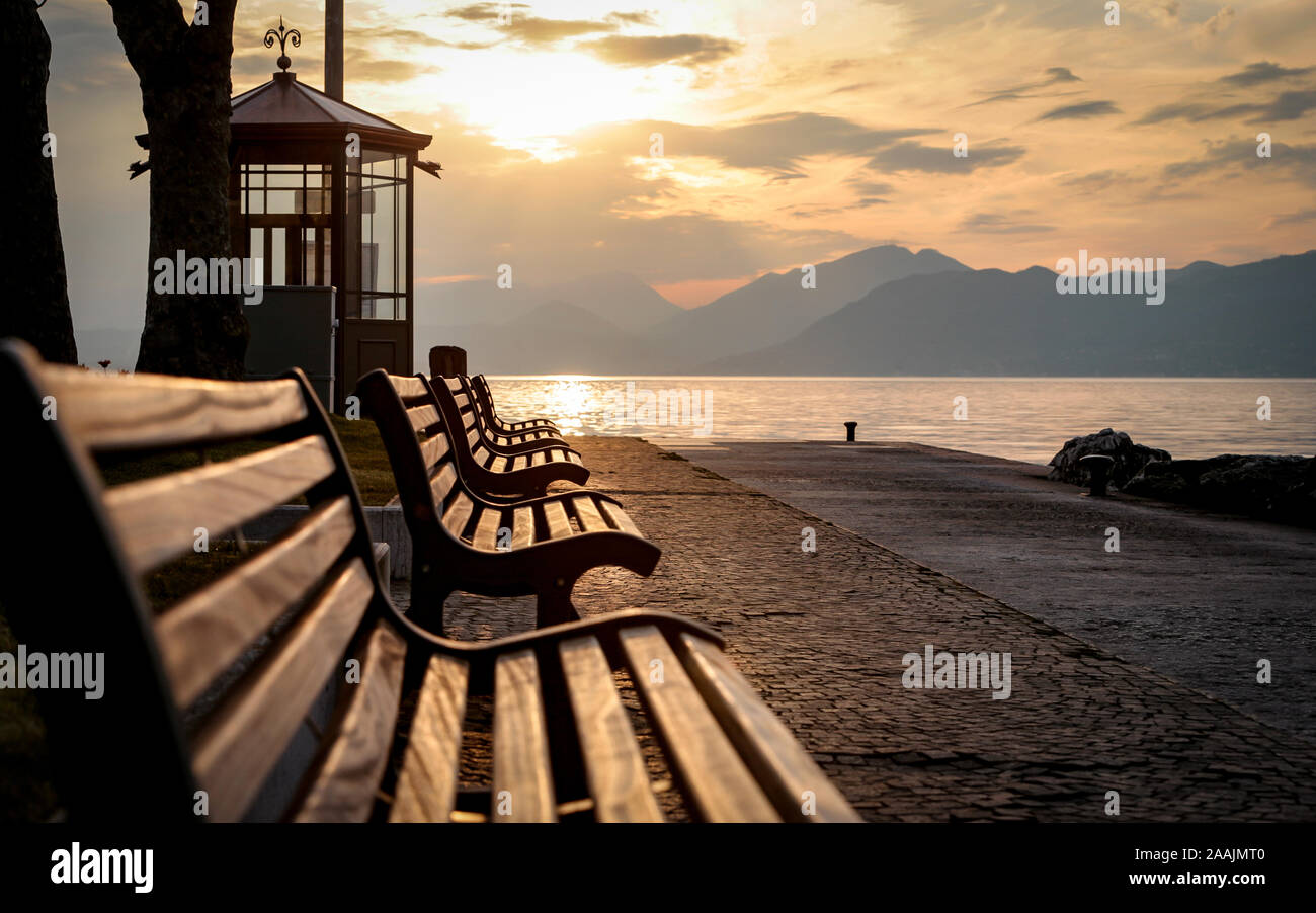 Lake Garda, Italy. A tranquil sunset view of benches looking over Lake Garda, Italy, towards the Italian Alps. Stock Photo
