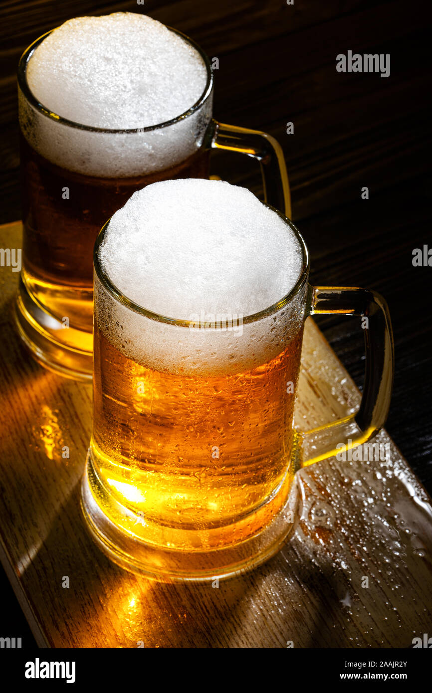 Two Light Beer Mugs with White Foam on Dark Wooden Table. View from Above Stock Photo