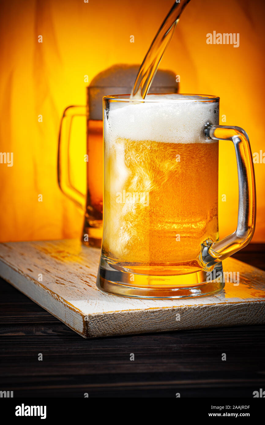 Pour Light Beer into Mugs. Light Beer Glass Mugs with White Foam on