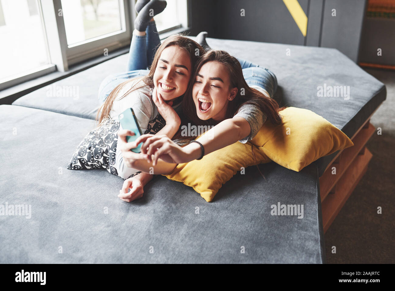 Two cute smiling twins sisters holding smartphone and making selfie 
