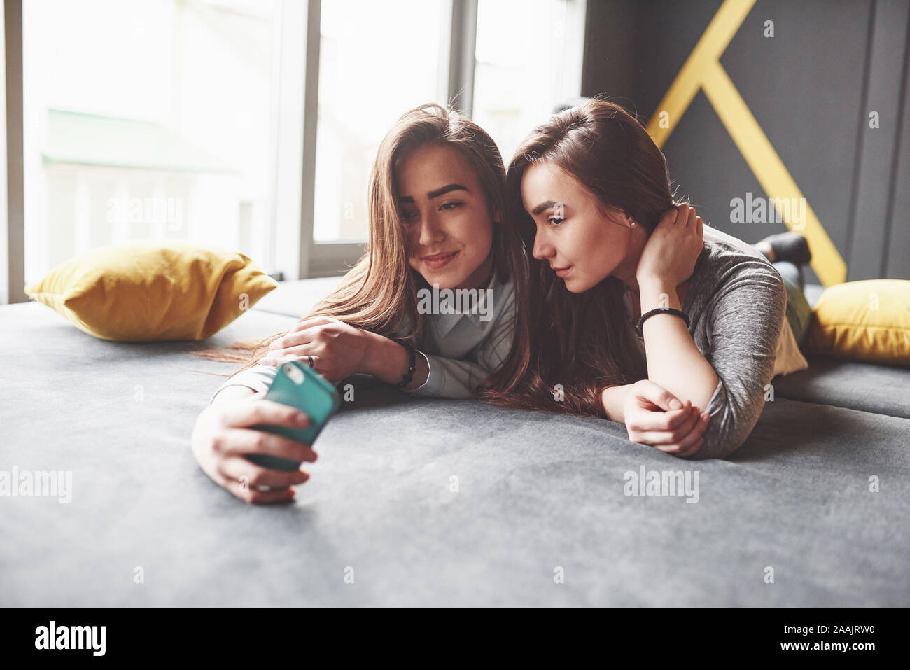 Two cute smiling twins sisters holding smartphone and making selfie 