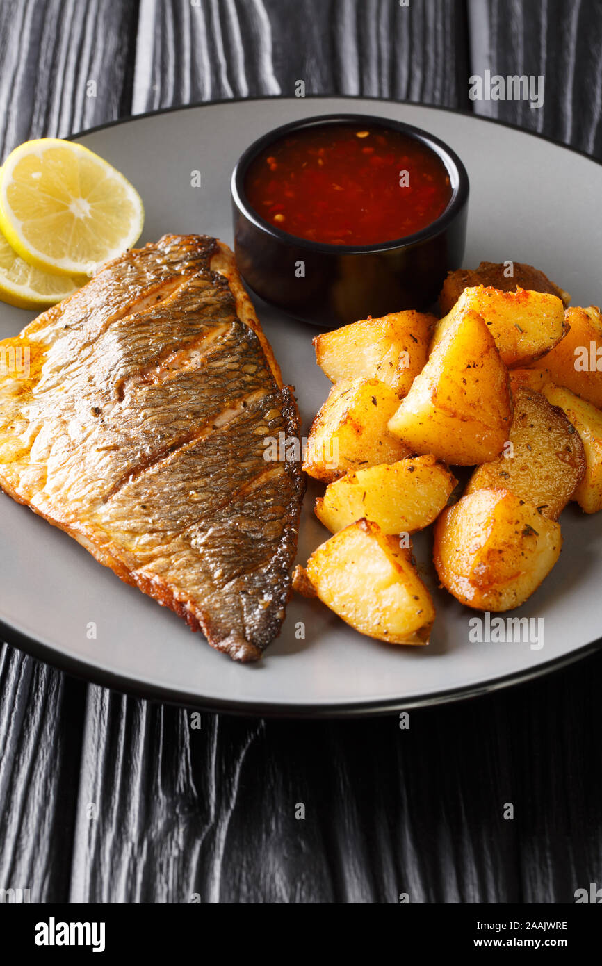 Grilled dorada filet with fried potatoes and sauces close-up on a plate on the table. vertical Stock Photo