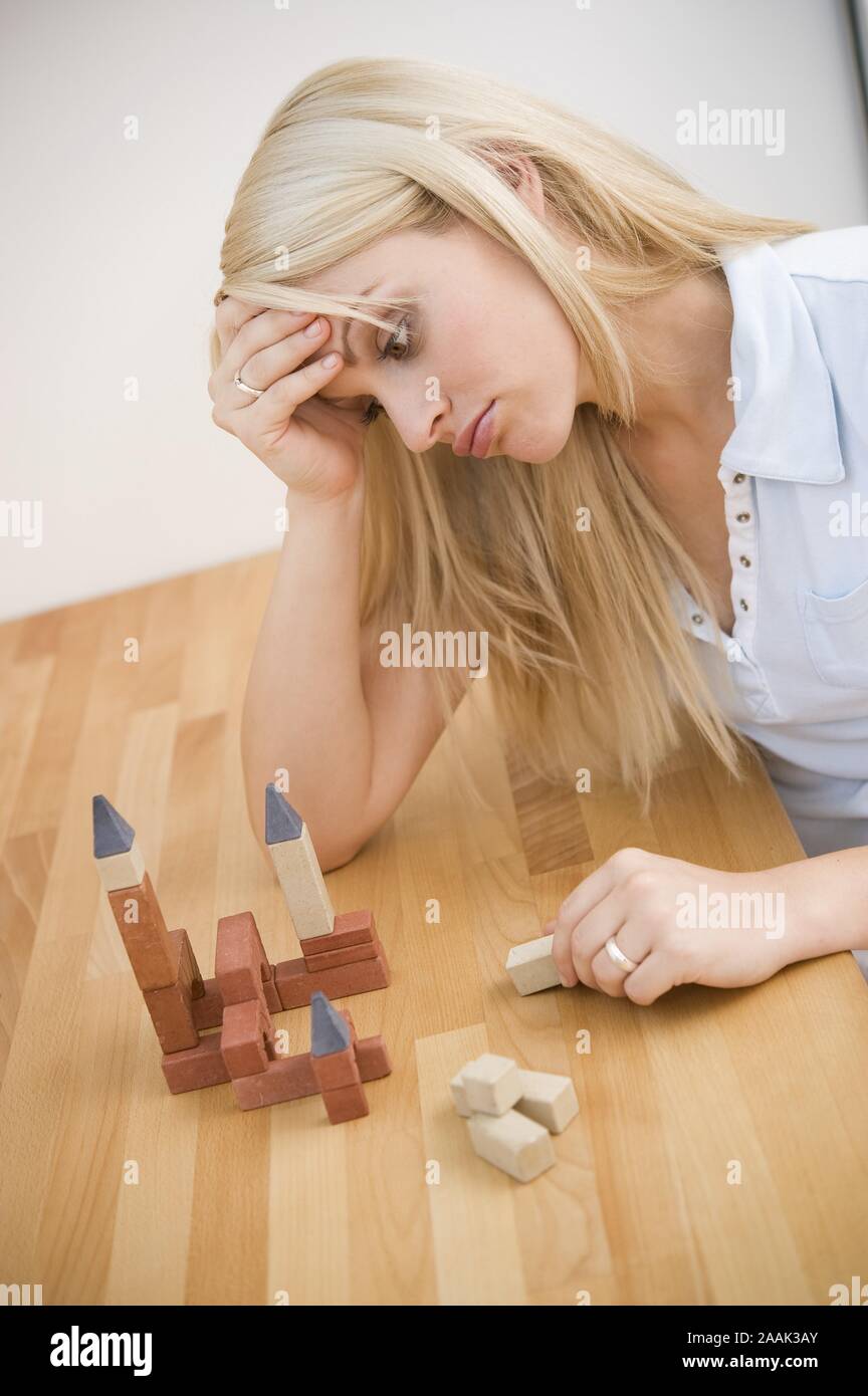 Nachdenkliche junge Frau schaut auf Bauklötze - Thoughtful young woman looking at building blocks Stock Photo