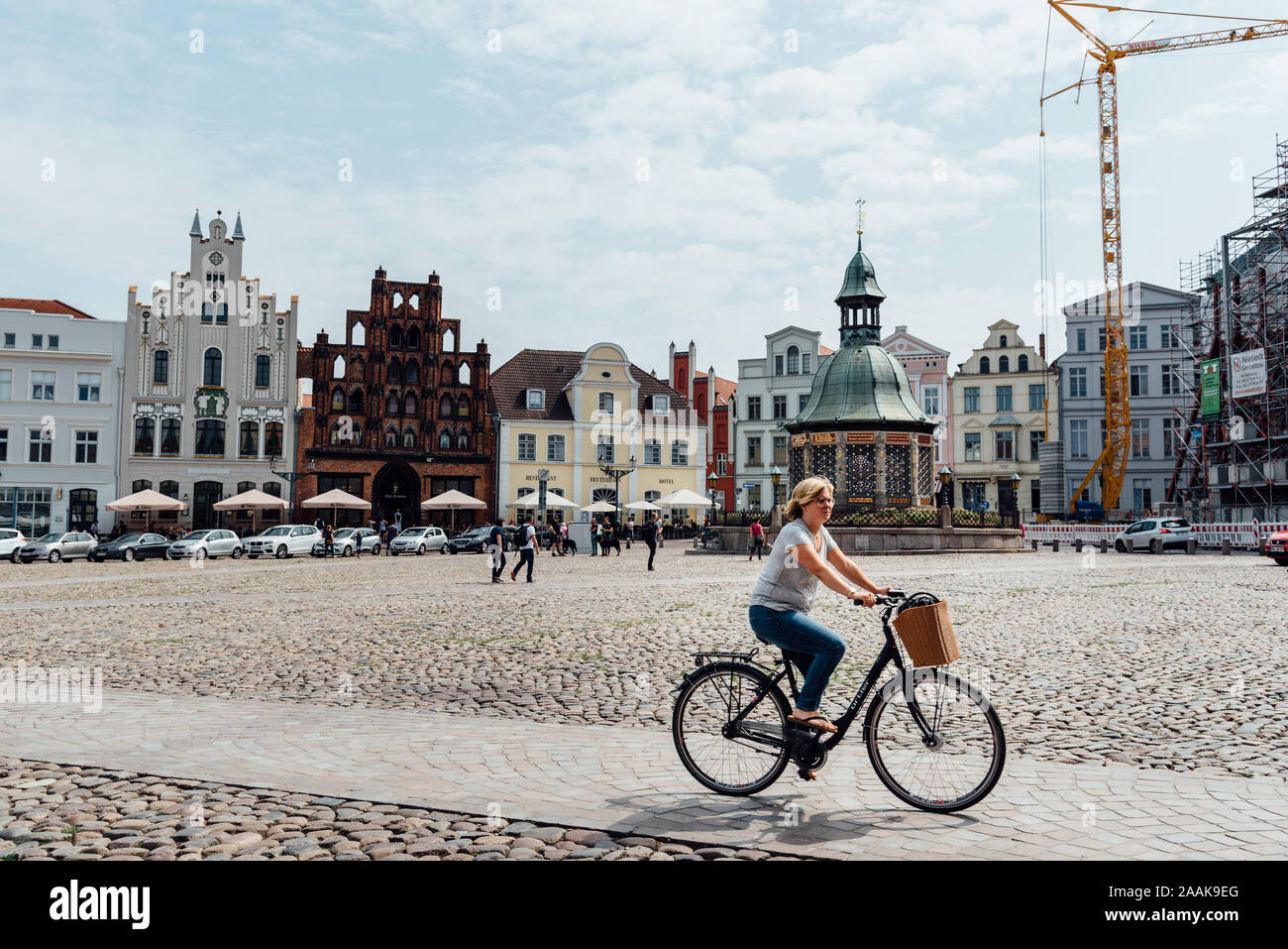 Wismar, Germany - August 2, 2019: Woman riding bicycle through square in historic centre. Wismar is a port and Hanseatic city in Northern Germany on t Stock Photo