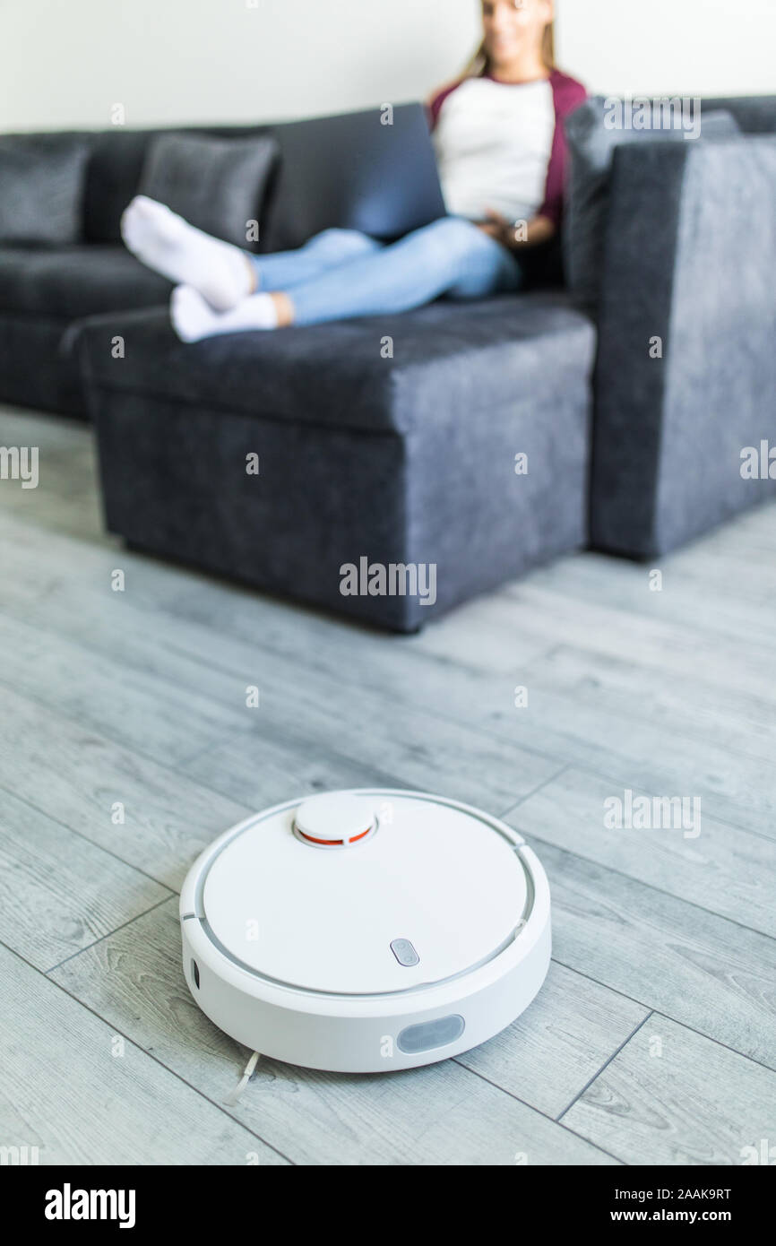 Robotic vacuum cleaner cleaning the room while woman resting on the sofa Stock Photo