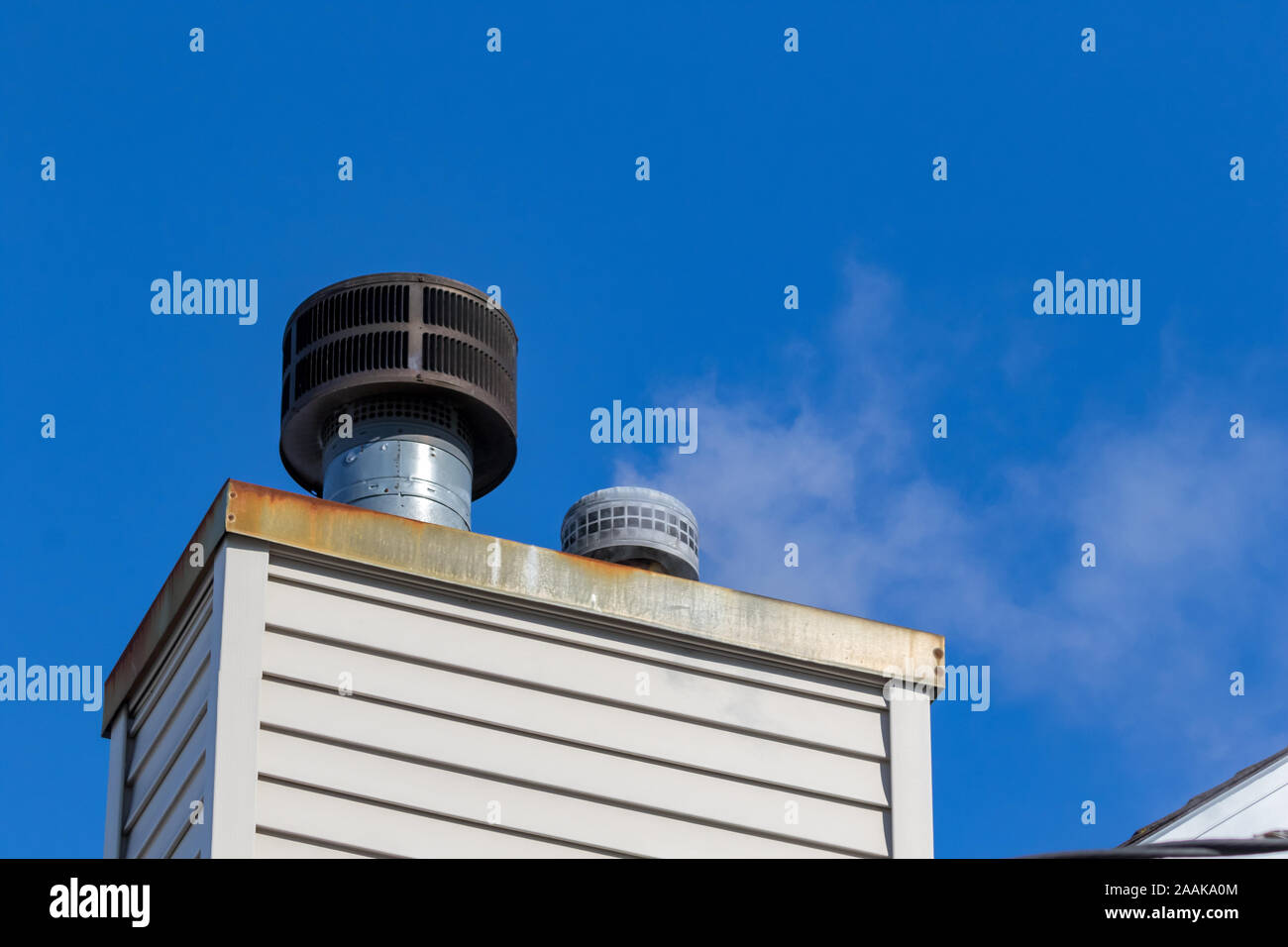 Looking up at white steam or smoke venting out of a house chimney flue vent pipe for furnace and water heater on a cold winter day. Stock Photo