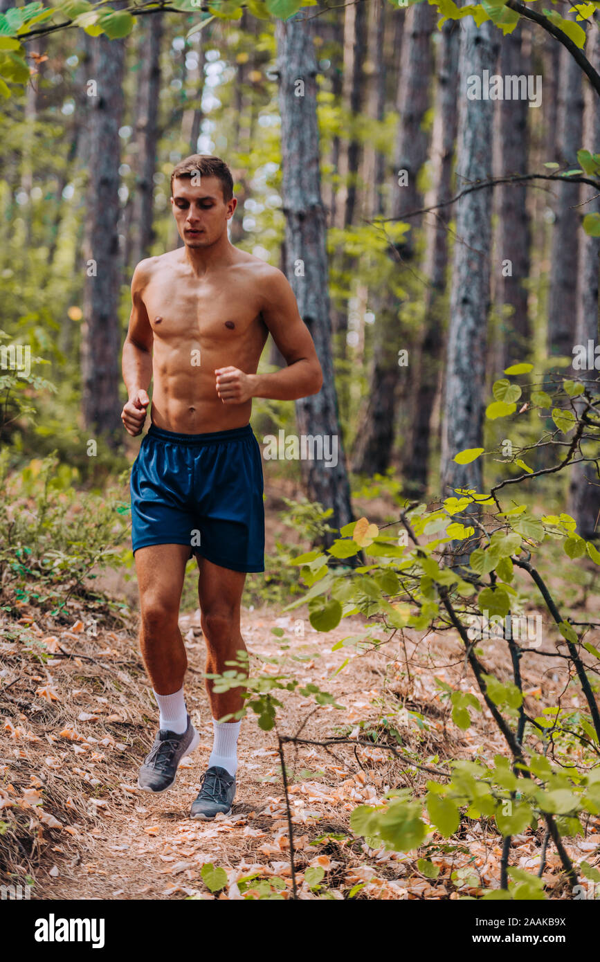Shirtless man jogging with headphones while sprinting on trail in mountains  against blue sky Stock Photo - Alamy