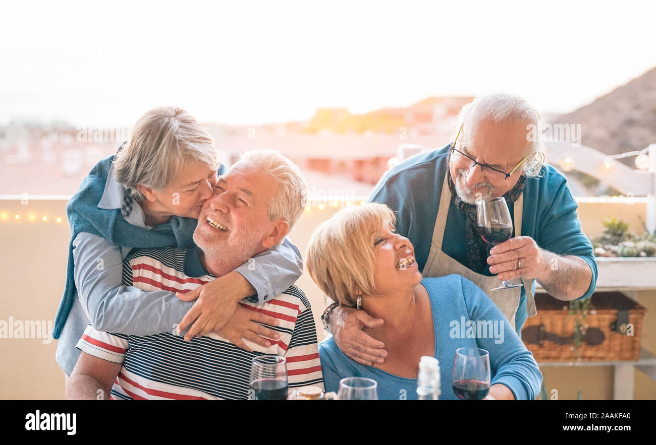Happy seniors couple having fun dining together on terrace - Romantic older people drinking wine and enjoying a sunny day on rooftop Stock Photo