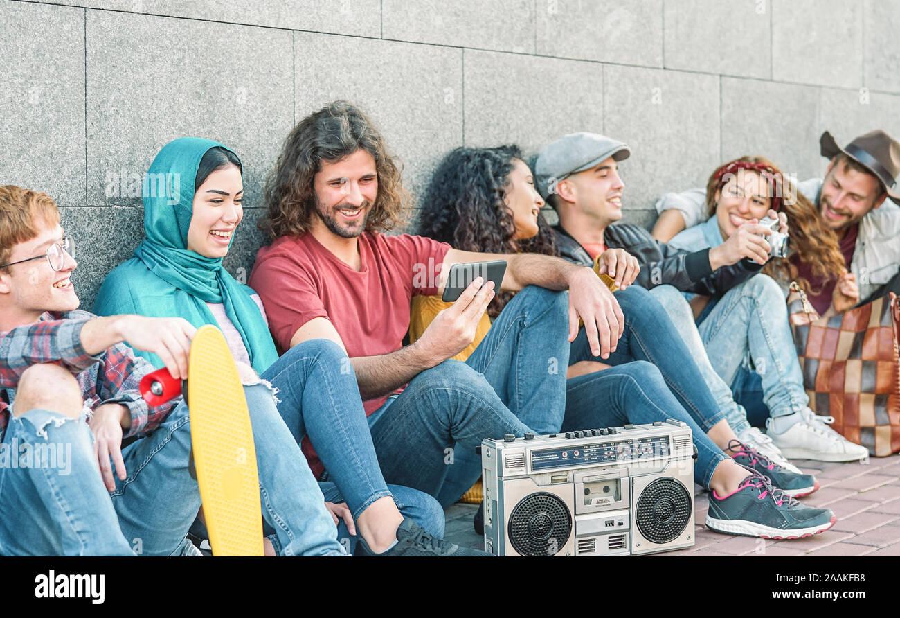 Group of diverse friends having fun outdoor - Millennial young people using mobile phones and listening music with vintage boombox stereo Stock Photo