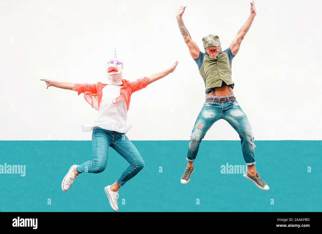 Happy seniors crazy couple wearing unicorn and t-rex mask while jumping outdoor - Mature trendy people having fun celebrating outside Stock Photo
