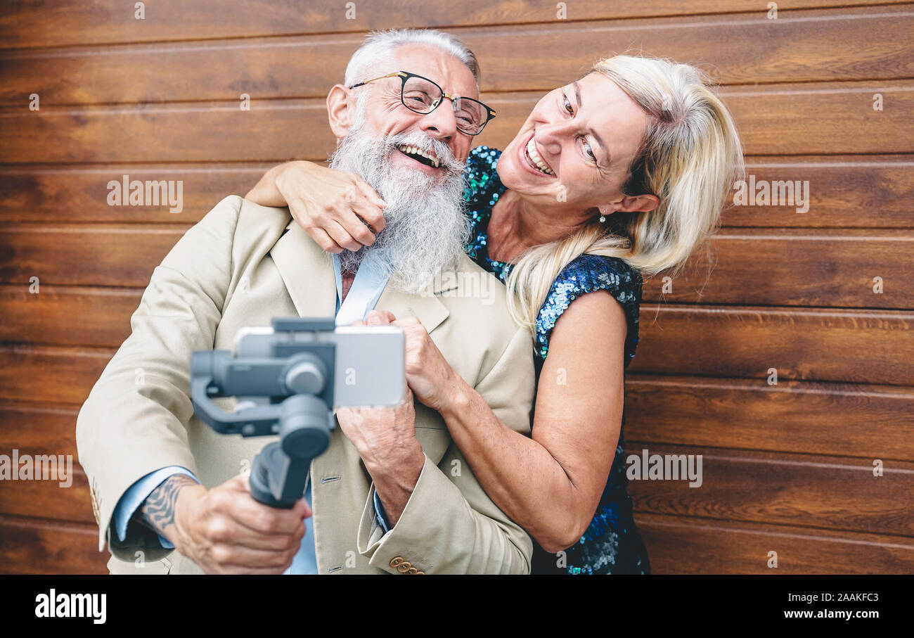 Happy seniors couple recording video with gimbal mobile phone outdoor - Mature fashion people having fun with new trends smartphone apps Stock Photo